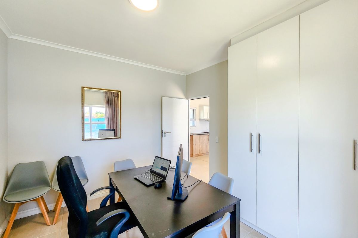 A well-maintained bedroom featuring neutral tiled flooring, built-in cupboards, and a clean, modern aesthetic with access to an adjacent room.