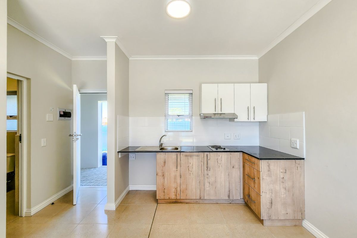 A clean, modern kitchen featuring light wood-finish cabinetry, dark countertops, a built-in hob with extractor, and neutral tiled flooring.