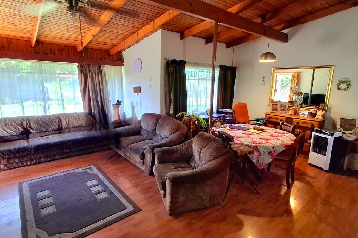 Open plan living and dining area featuring exposed timber beam ceilings, laminate flooring, and large windows with security bars.