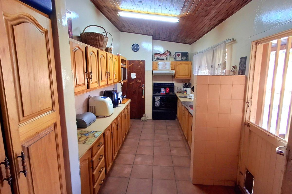 A functional kitchen featuring timber cabinetry, tiled flooring, a timber-paneled ceiling, and a freestanding oven with an integrated extractor fan.