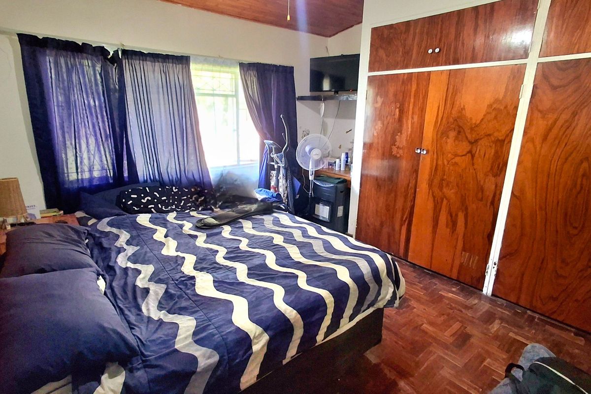 A bedroom featuring parquet flooring, a timber ceiling, and built-in wooden cupboards, offering a functional space with potential for cosmetic updates.