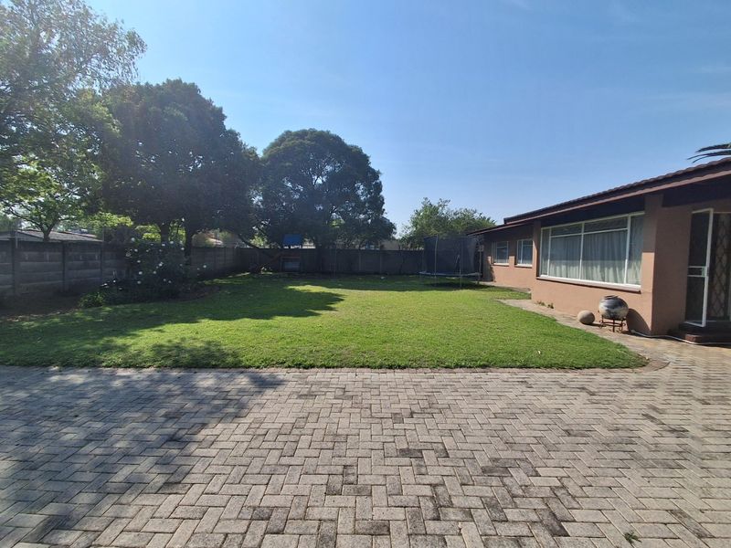 A spacious rear garden featuring a paved patio area, a well-maintained lawn, and secure perimeter walling.