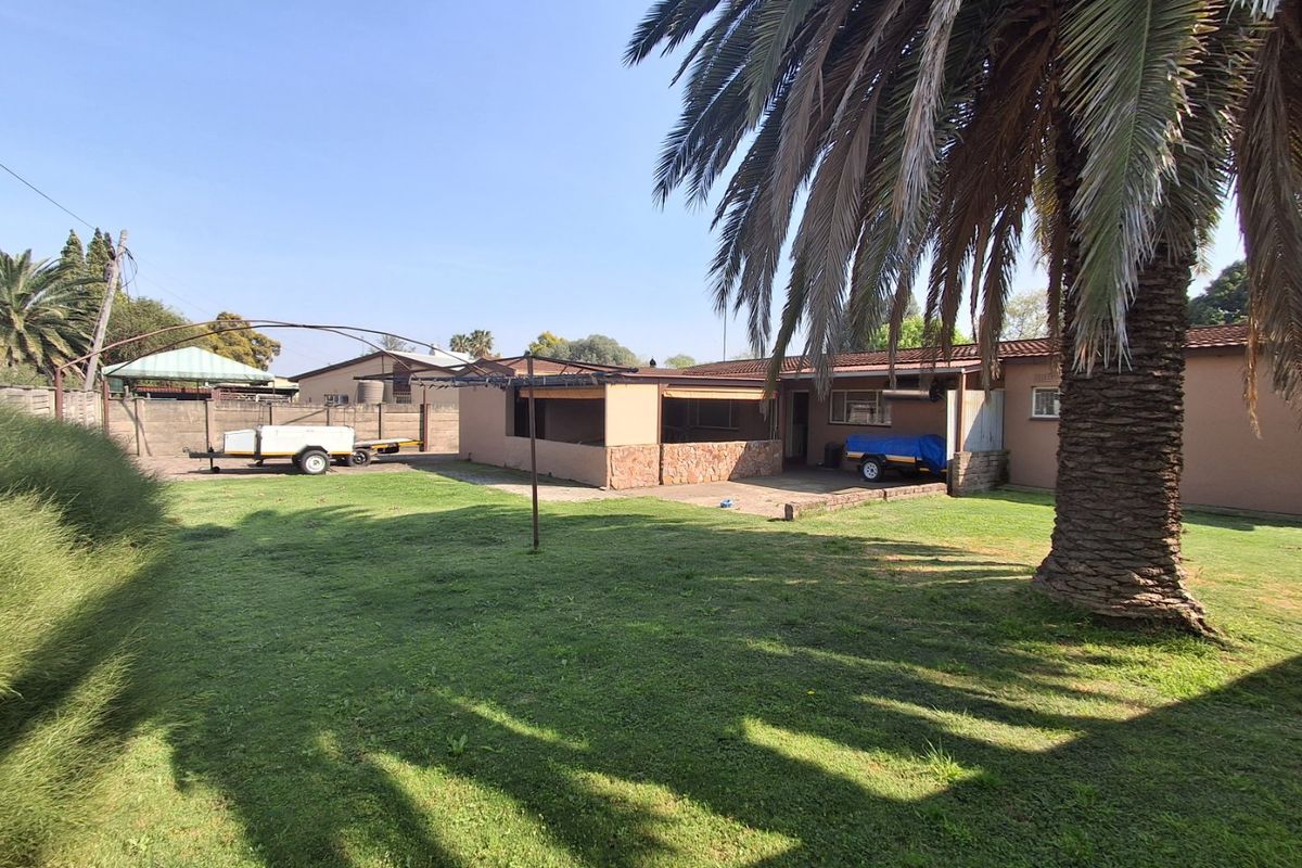 Rear view of the property featuring a spacious lawn, a covered patio area with stone cladding, and a secure brick boundary wall.