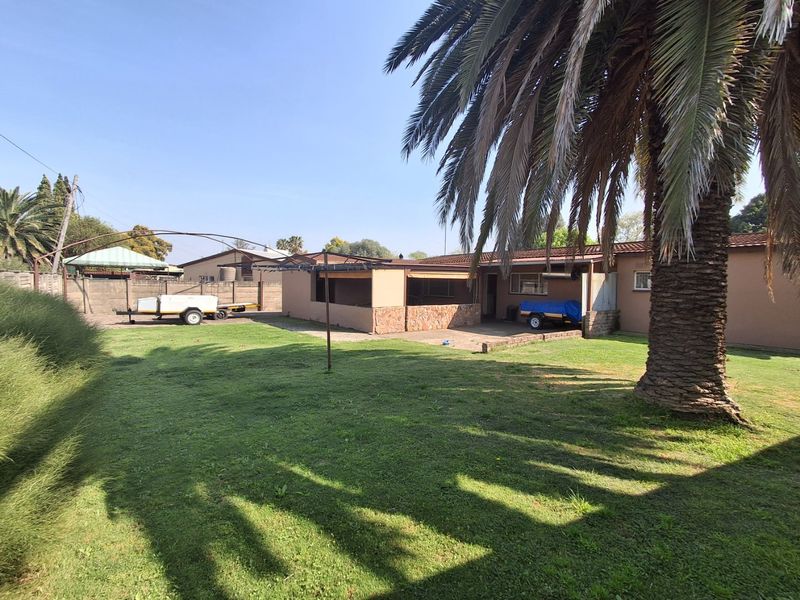 Rear view of the property featuring a spacious lawn, a covered patio area with stone cladding, and a secure brick boundary wall.