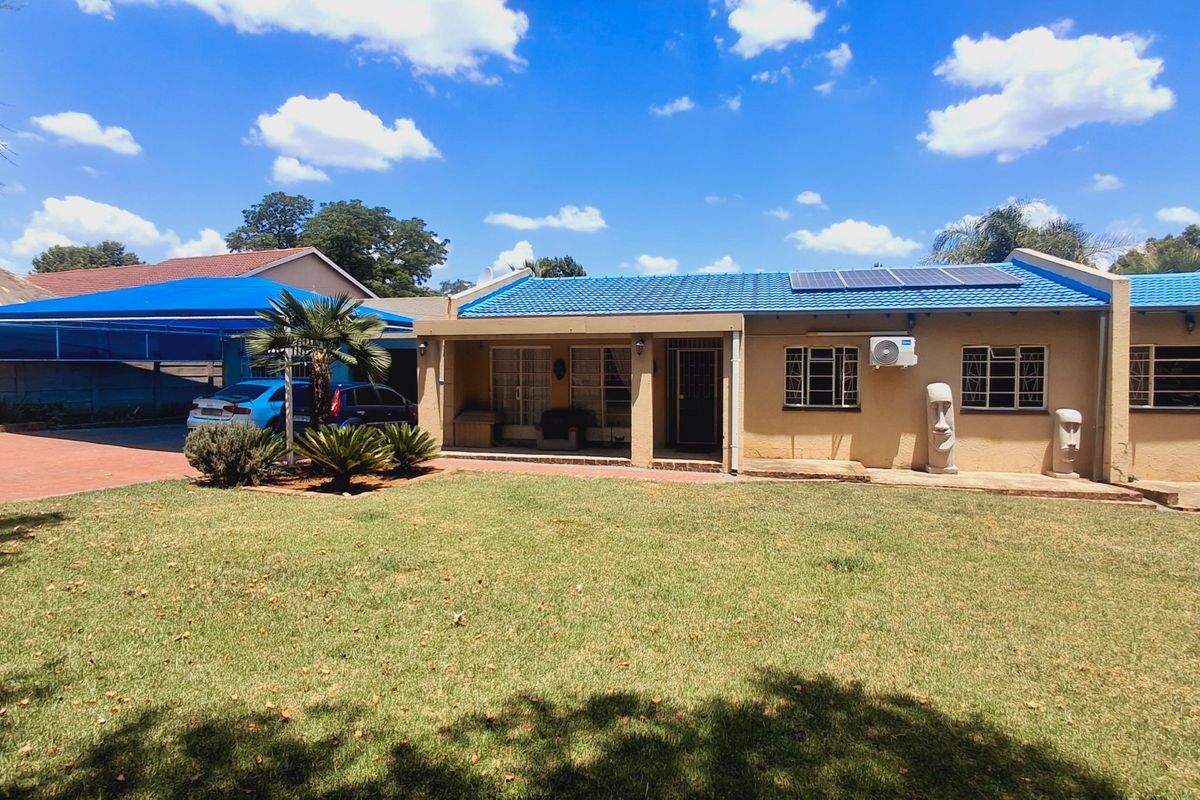 Rear view of a single-story house featuring a blue tiled roof with solar panels, a covered patio, and a spacious lawn area.
