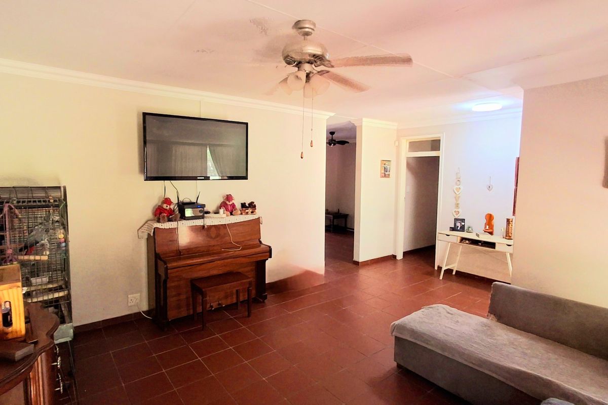 A living room featuring tiled flooring, coved cornicing, and a ceiling fan, with visible water staining on the ceiling requiring attention.