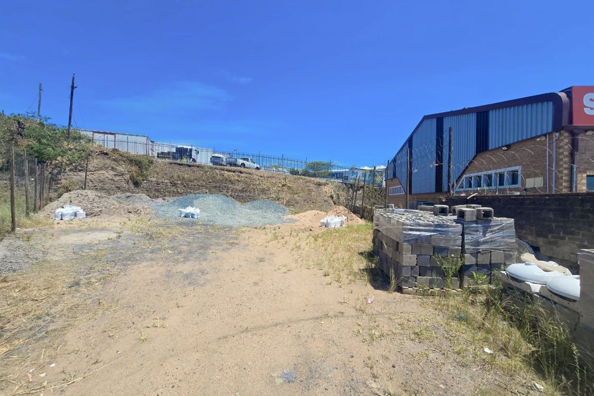 Rear exterior area of a commercial property featuring a retaining wall, security fencing with razor wire, and unpaved ground with construction materials.