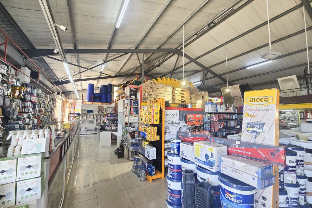 A spacious commercial retail warehouse featuring high exposed steel ceilings, tiled flooring, and extensive metal shelving units for product display.