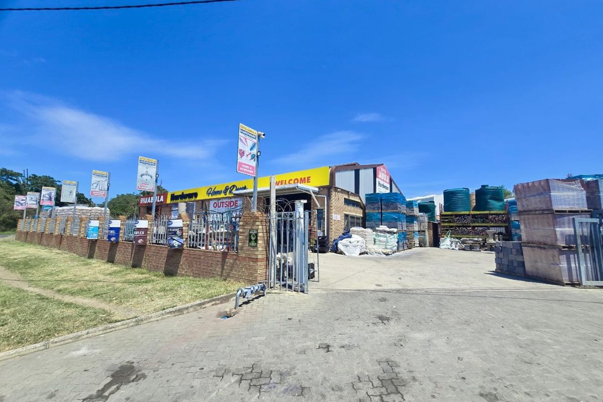 Front exterior view of a commercial hardware store featuring a paved driveway, brick perimeter wall, security fencing, and prominent signage.
