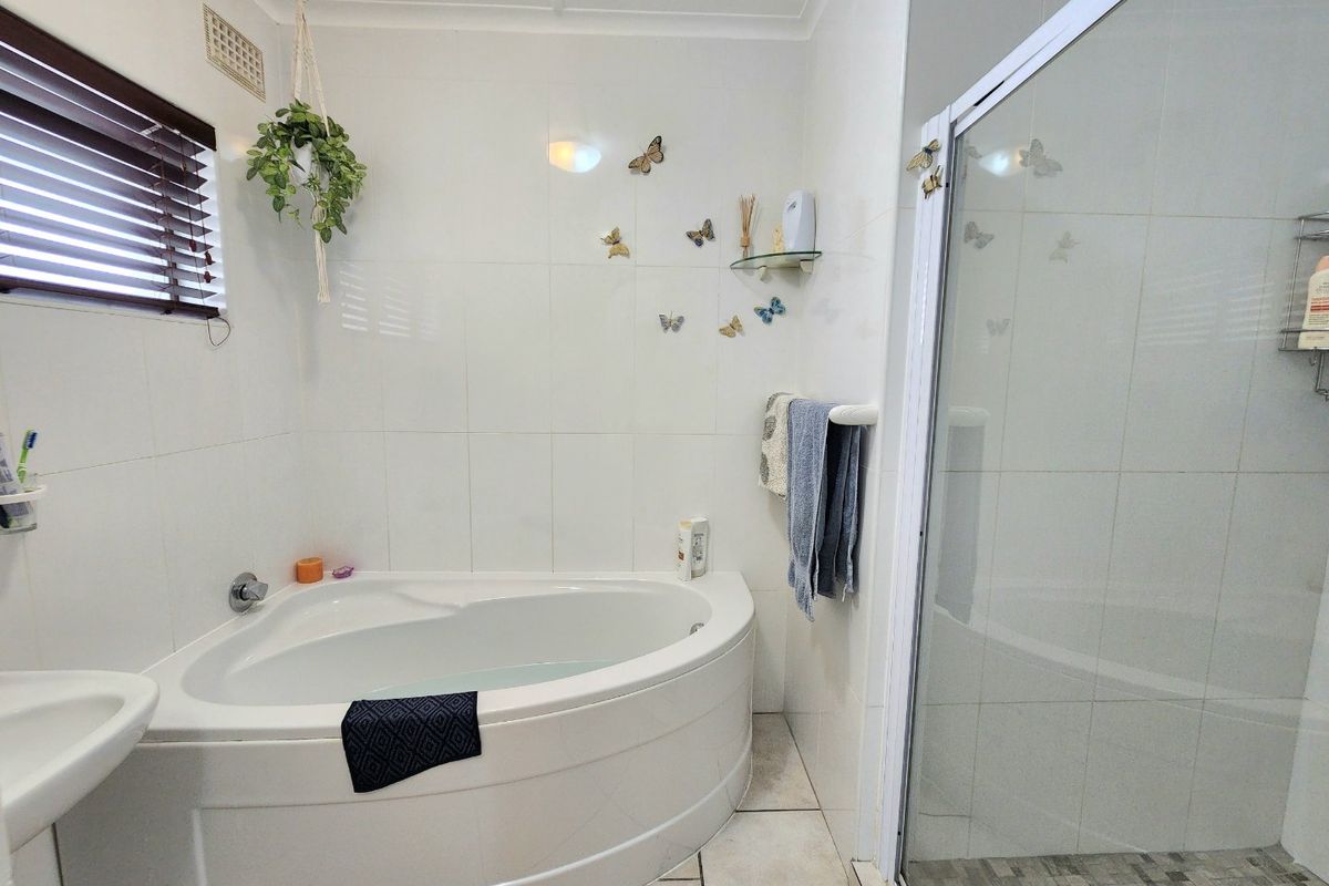 A functional bathroom featuring a corner bathtub, separate shower enclosure, and neutral wall tiling, offering a clean and practical layout.
