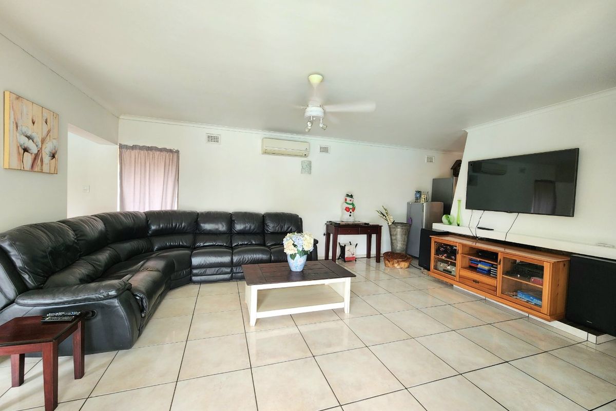 Spacious living room featuring neutral tiled flooring, a ceiling fan, and a wall-mounted split-system air conditioner.