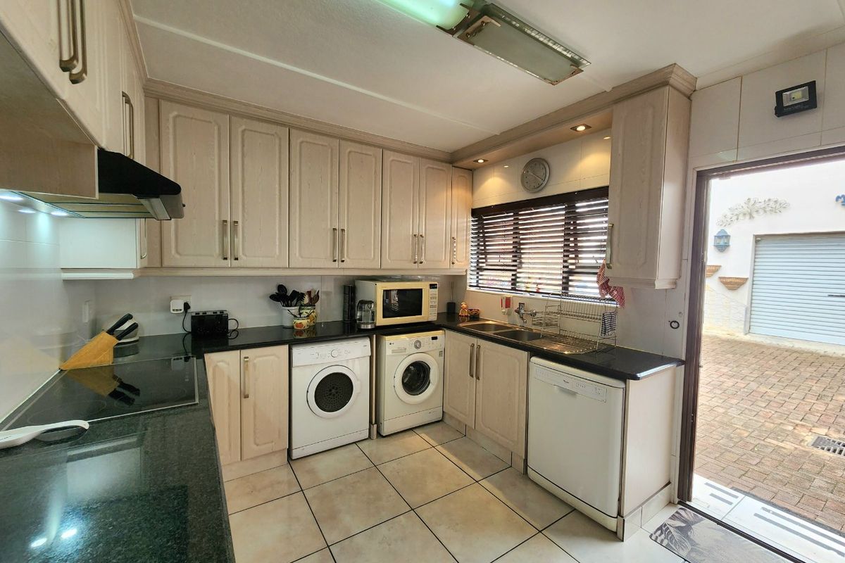 Functional kitchen featuring light-toned cabinetry, granite countertops, tiled flooring, and direct access to the exterior paved area.