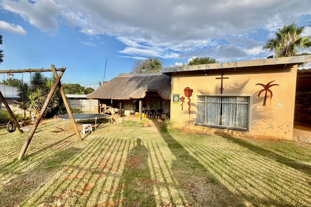 Rear view of the property featuring a thatched roof section, concrete patio area, and a spacious garden with perimeter walling.