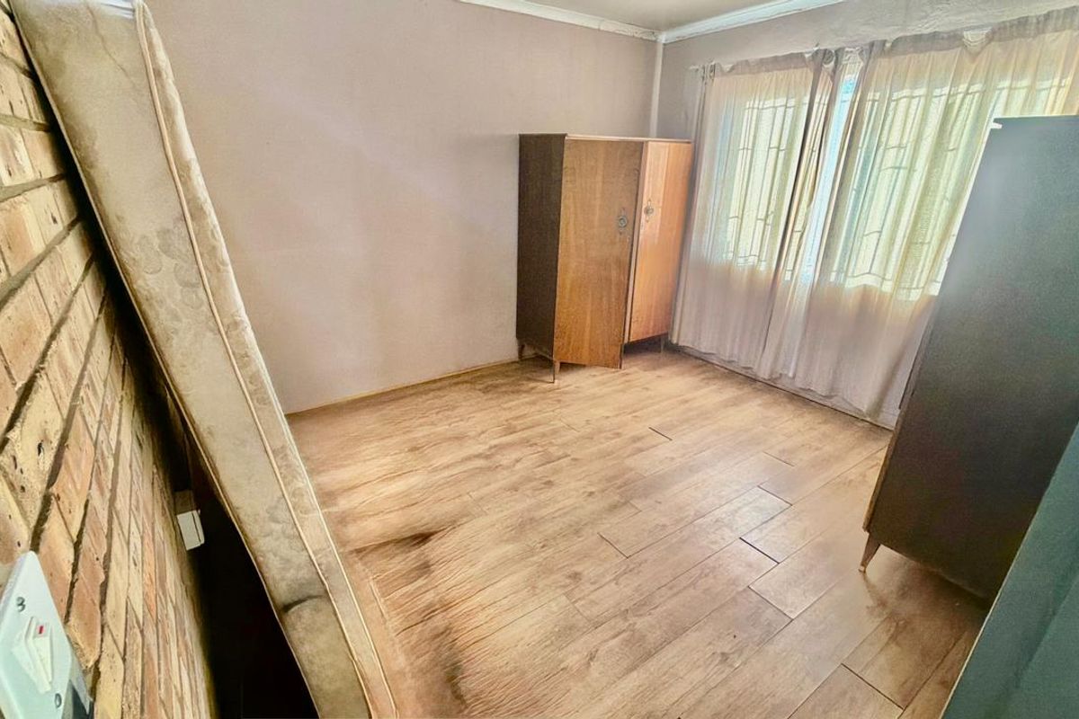 A bedroom featuring exposed brickwork and wood-look tile flooring, offering a blank canvas for renovation and interior design updates.
