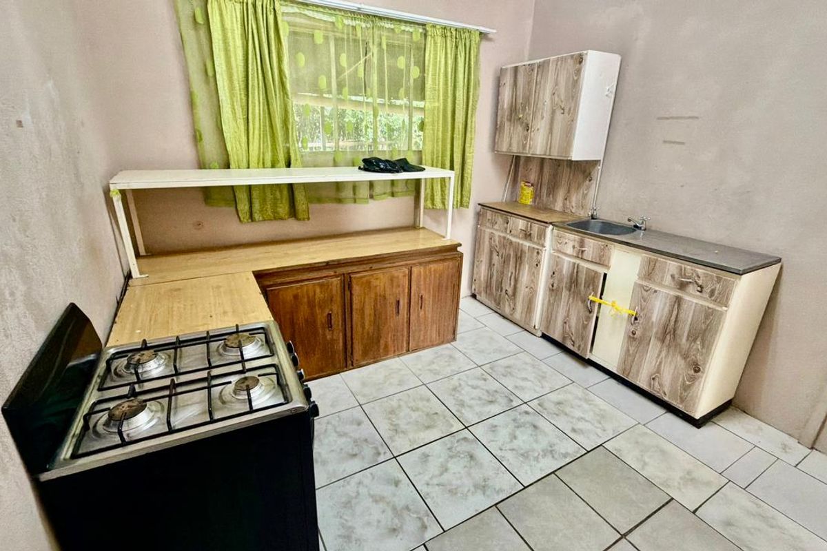 A functional kitchen featuring tiled flooring, wooden cabinetry, a stainless steel sink, and a gas stove, offering potential for modernization and cosmetic updates.