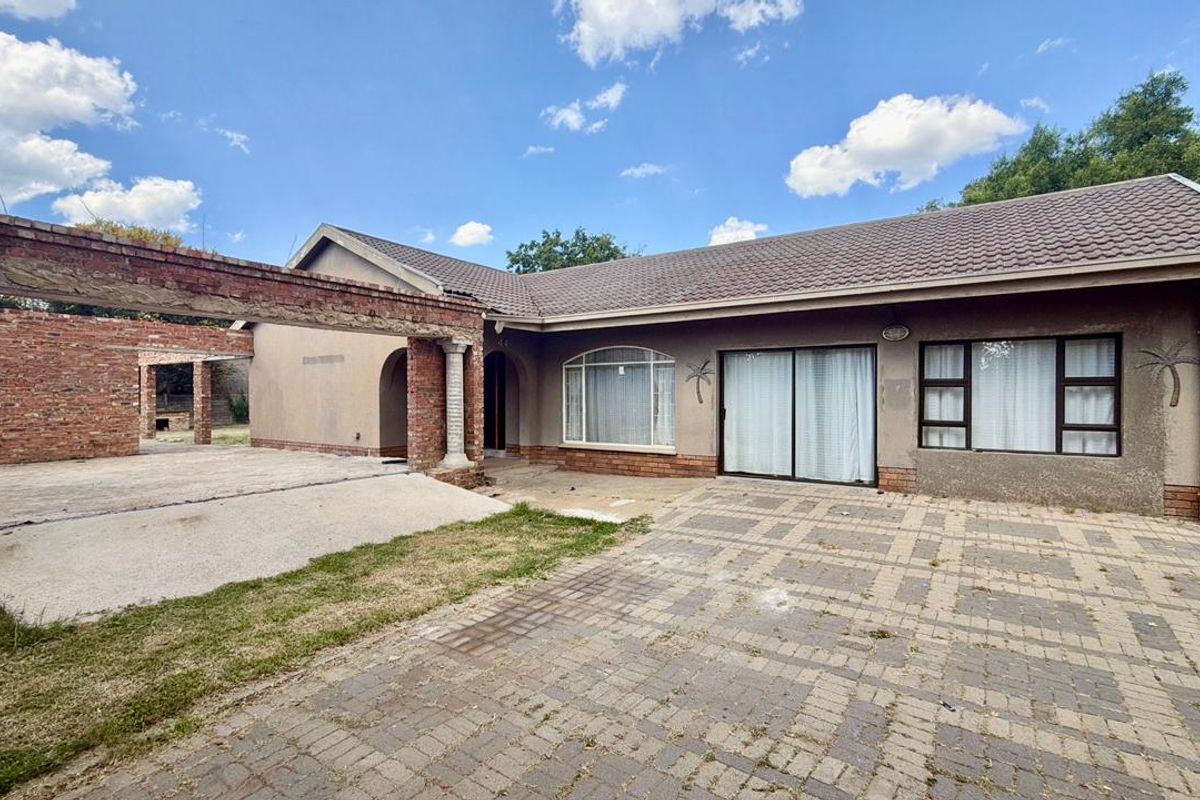 Rear exterior view of the property featuring a paved driveway, a brick pergola structure, and sliding glass doors leading into the home.