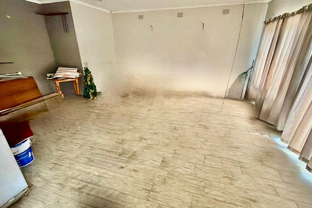 An empty living room featuring tiled flooring and neutral walls, currently showing signs of wear and surface staining requiring maintenance.
