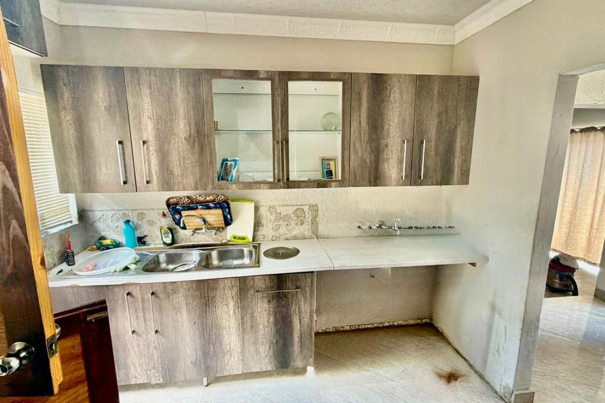 A functional kitchen area featuring wood-look laminate cabinetry, a double stainless steel sink, and tiled flooring, currently requiring some finishing and maintenance.