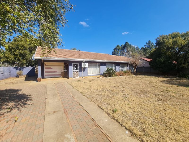 Front elevation of a single-story house featuring a paved driveway, attached garage, and established garden area.