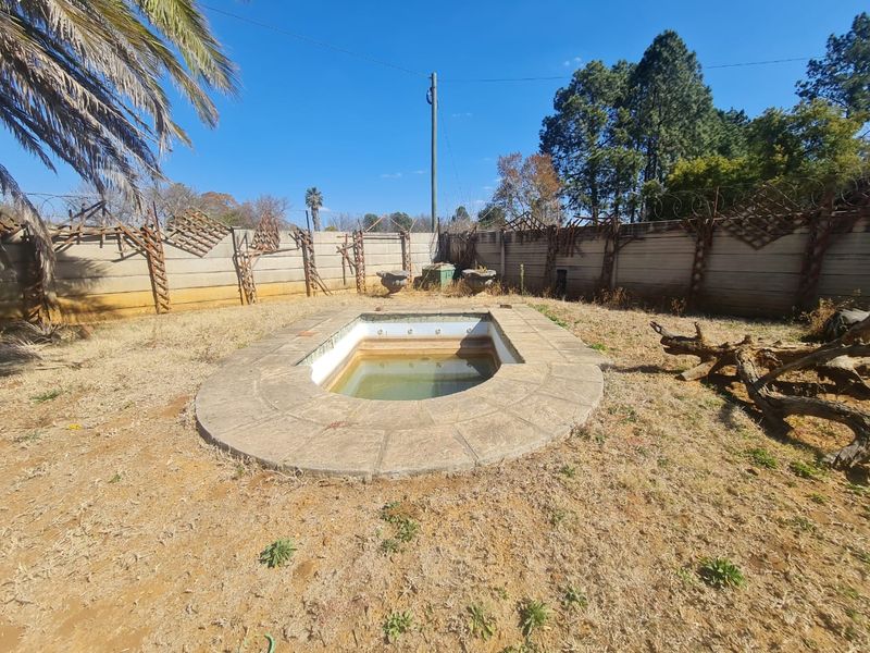 Outdoor pool area featuring a concrete surround and perimeter wall with security fencing, currently requiring significant maintenance and landscaping.