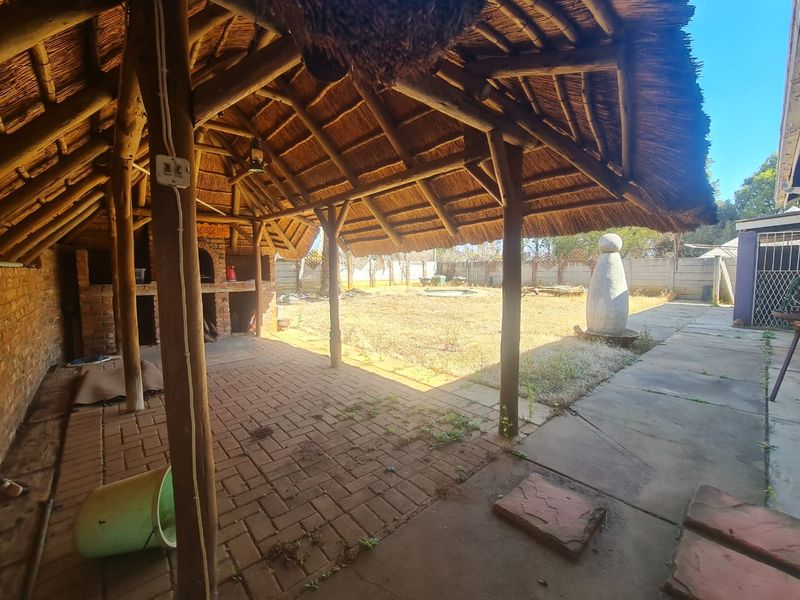 Covered outdoor patio area featuring a traditional thatched roof, built-in brick braai, and paved flooring overlooking the rear garden.