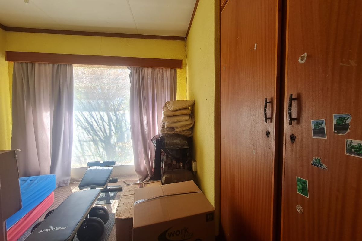 A bedroom featuring built-in wooden cupboards and a large window, currently used as a storage and exercise space.