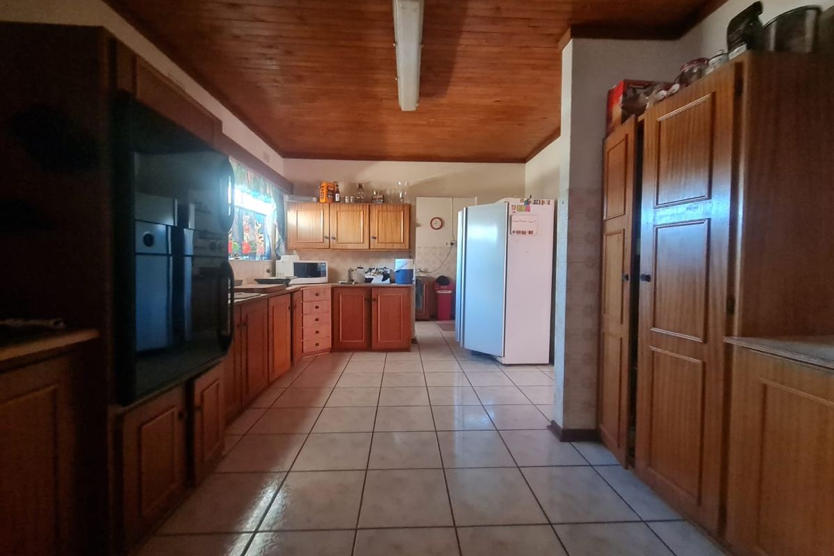 A spacious kitchen featuring extensive wooden cabinetry, tiled flooring, and a traditional wooden ceiling, offering a functional layout with ample storage space.