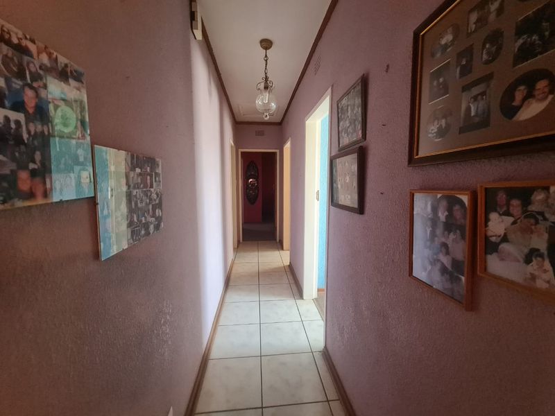 A narrow residential hallway featuring tiled flooring and a central ceiling light fixture, providing access to multiple rooms.