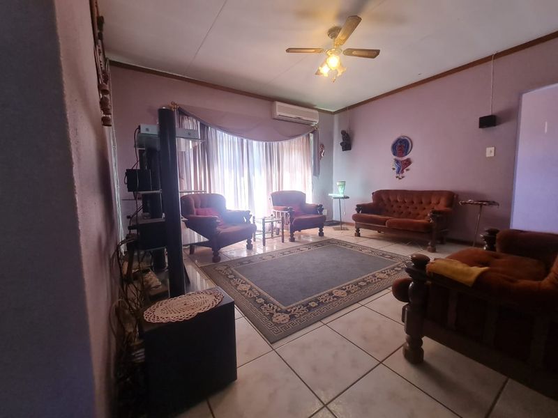 A living room featuring tiled flooring, a ceiling fan, and a wall-mounted air conditioning unit, with potential for cosmetic updates.