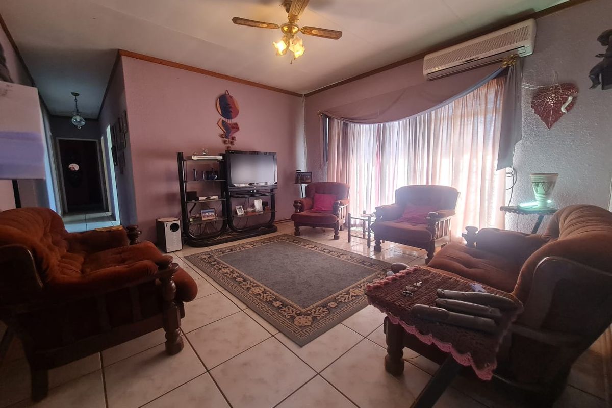 A living room featuring tiled flooring, a ceiling fan, and a wall-mounted air conditioning unit, offering a functional space with potential for modernization.