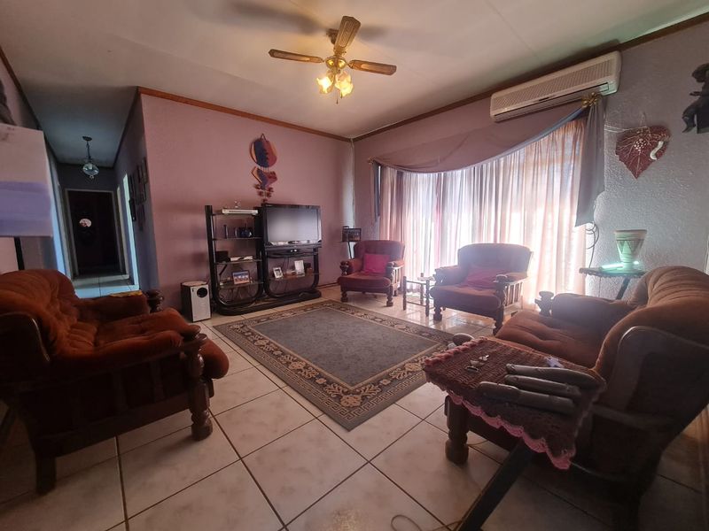 A living room featuring tiled flooring, a ceiling fan, and a wall-mounted air conditioning unit, offering a functional space with potential for modernization.
