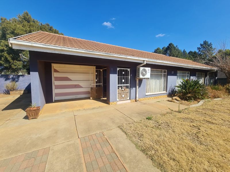 Front exterior view of a single-story house featuring a tiled roof, paved driveway, integrated garage, and security gate access.