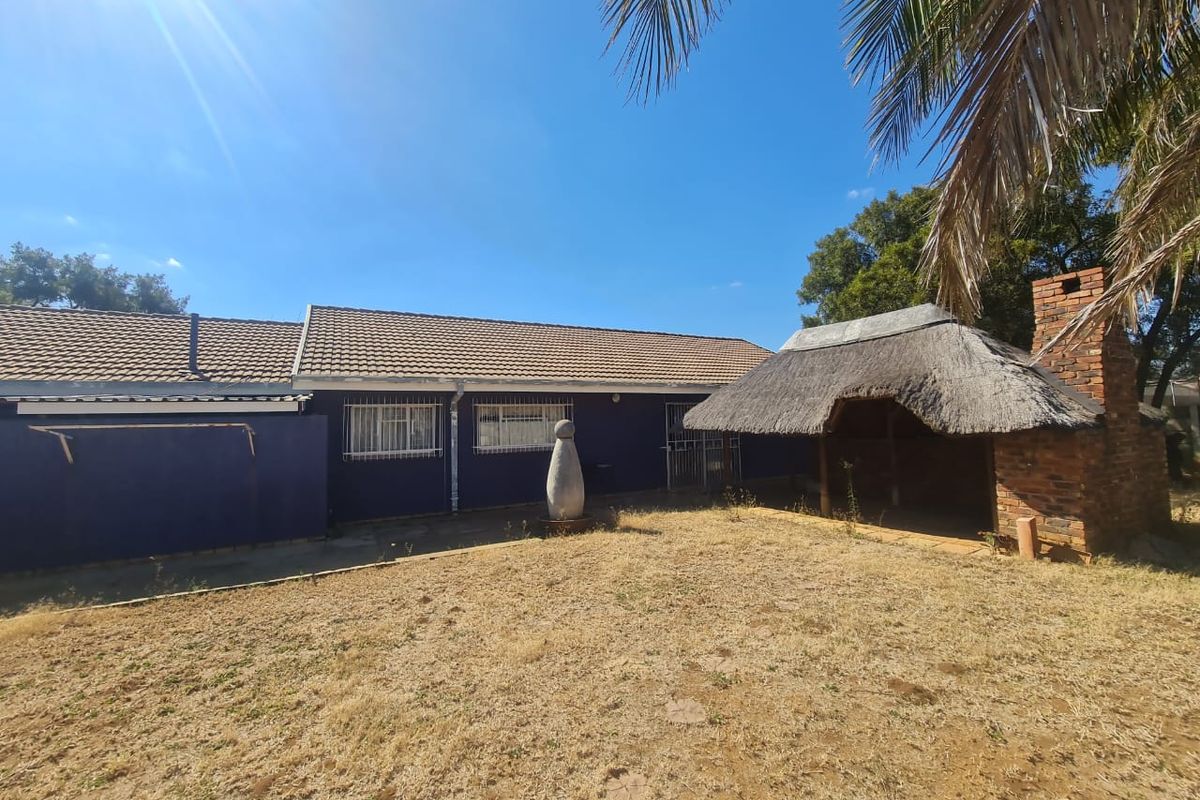 Rear view of the property featuring a thatched lapa with a brick fireplace and a large garden area.