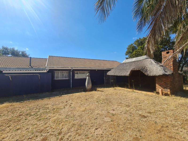 Rear view of the property featuring a thatched lapa with a brick fireplace and a large garden area.