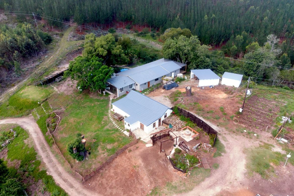 Aerial view of a farm property featuring multiple buildings with metal roofs, a swimming pool, and surrounding rural landscape.