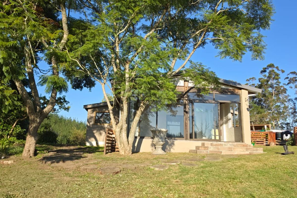 Rear view of the farm dwelling featuring large glass sliding doors, stone steps, and a timber-framed structure set within a spacious garden.