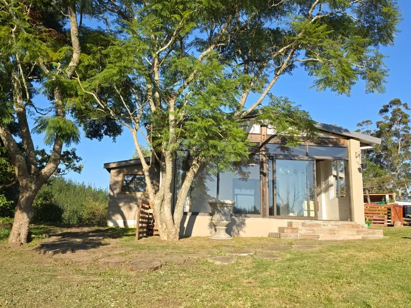 Rear view of the farm dwelling featuring large glass sliding doors, stone steps, and a timber-framed structure set within a spacious garden.