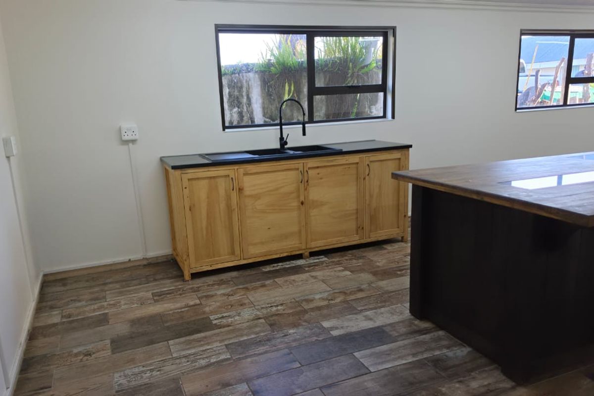 A clean, modern kitchen area featuring wooden cabinetry, a dark countertop with a black sink, and wood-look tile flooring in an open-plan space.