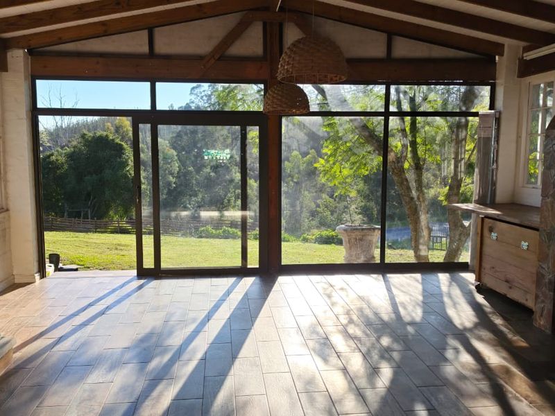 Spacious enclosed patio featuring exposed timber beams, tiled flooring, a built-in stone fireplace, and a wood-burning stove with expansive garden views.