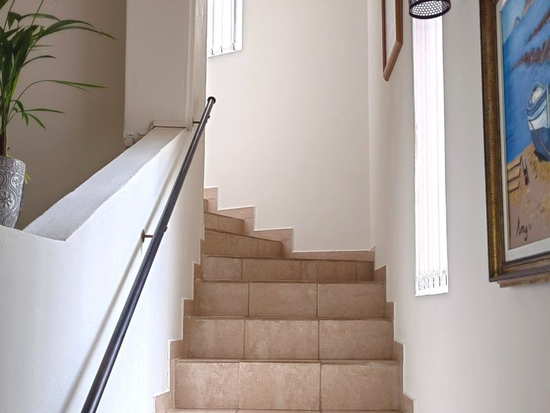 A bright, tiled staircase featuring a modern metal handrail and wall-mounted lighting, leading to an upper level.