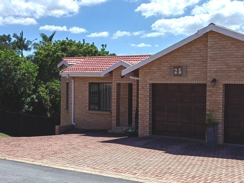 Front view of a well-maintained face brick house featuring a double garage, tiled roof, and a spacious paved driveway.