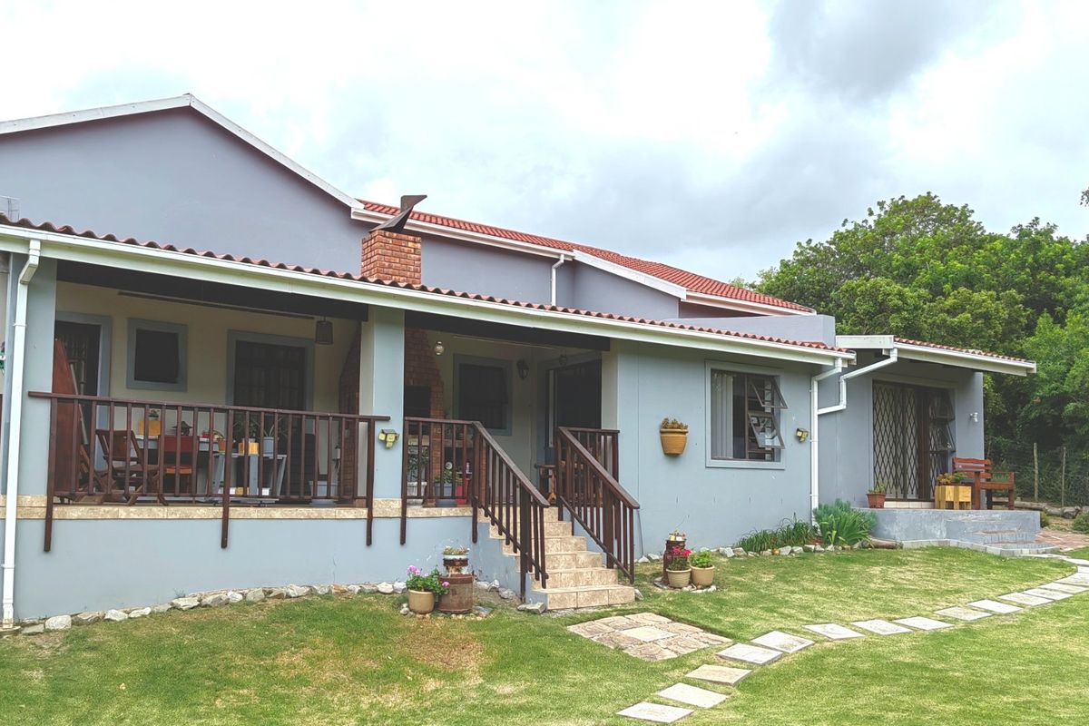 Rear view of the house featuring a covered patio with a built-in brick braai, timber railings, and a well-maintained garden with a paved walkway.