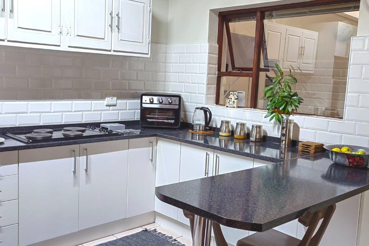 A well-maintained kitchen featuring white cabinetry, dark granite countertops, a subway tile backsplash, and a convenient breakfast bar with tiled flooring.