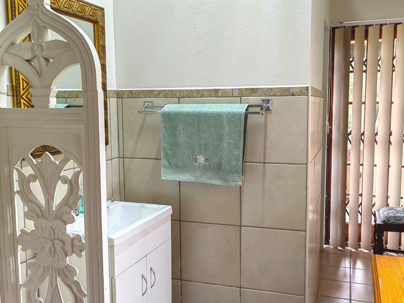 A functional bathroom featuring a vanity cabinet with basin, tiled walls and flooring, and a timber ceiling with access to an outdoor area.