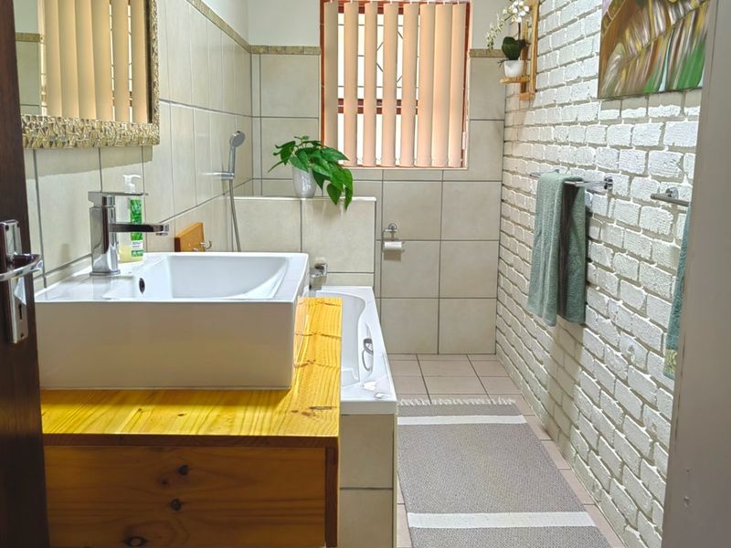 A well-maintained bathroom featuring a vessel sink on a timber vanity, a built-in bathtub, and a distinctive exposed brick feature wall.