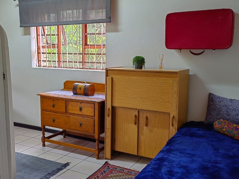 A bedroom featuring tiled flooring, a timber-paneled ceiling, and a window fitted with security bars and a roller blind.