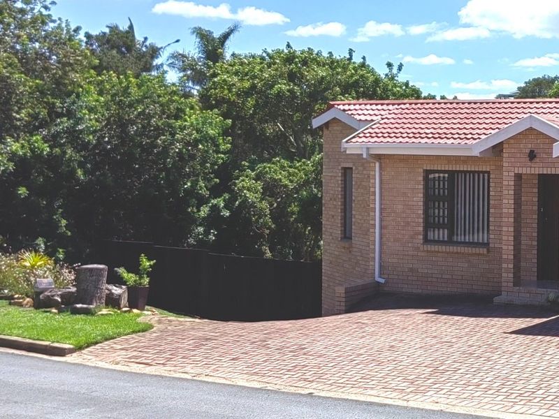 A well-maintained face-brick house exterior featuring a tiled roof, paved driveway, and secure window bars, set in a landscaped residential environment.