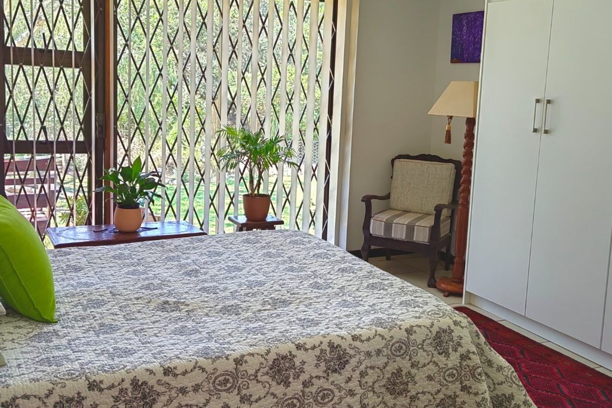 A bedroom featuring built-in wardrobes, tiled flooring, and a sliding glass door with a security gate leading to the exterior.
