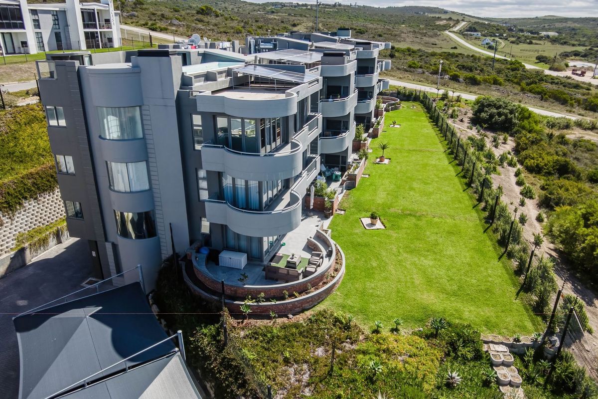 Aerial view of a modern apartment complex featuring curved balconies, solar panels, ground-floor patios, and a well-maintained communal lawn area.