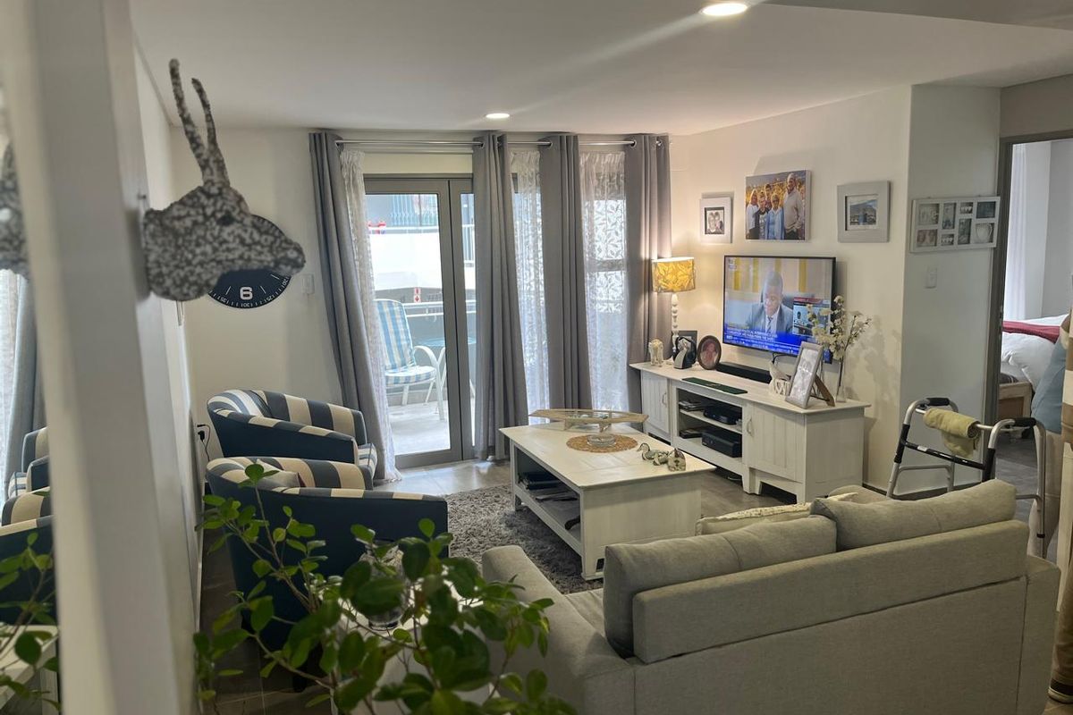 A well-maintained living room featuring tiled flooring, recessed downlighting, and a sliding glass door providing access to the balcony.